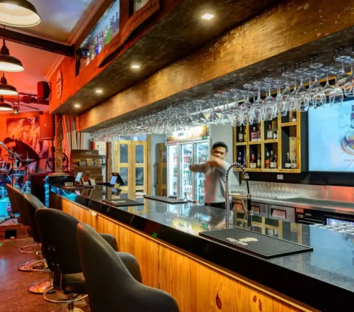 Rah Nah Bar in Lovina features a beautifully stocked counter serving international cocktails, premium wine, and spirits, complete with a bartender mixing drinks right next to the live music stage.