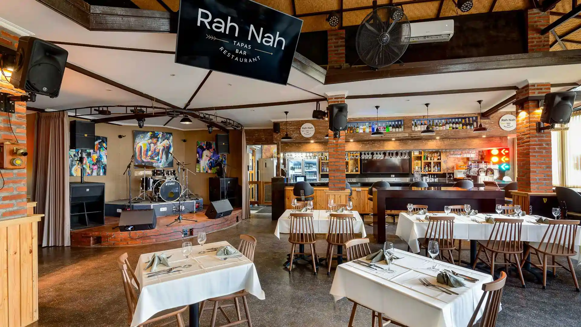 Interior view of Rah Nah Tapas featuring a rustic brick bar, performance stage for live bands, and cozy dining tables in Lovina, Bali.